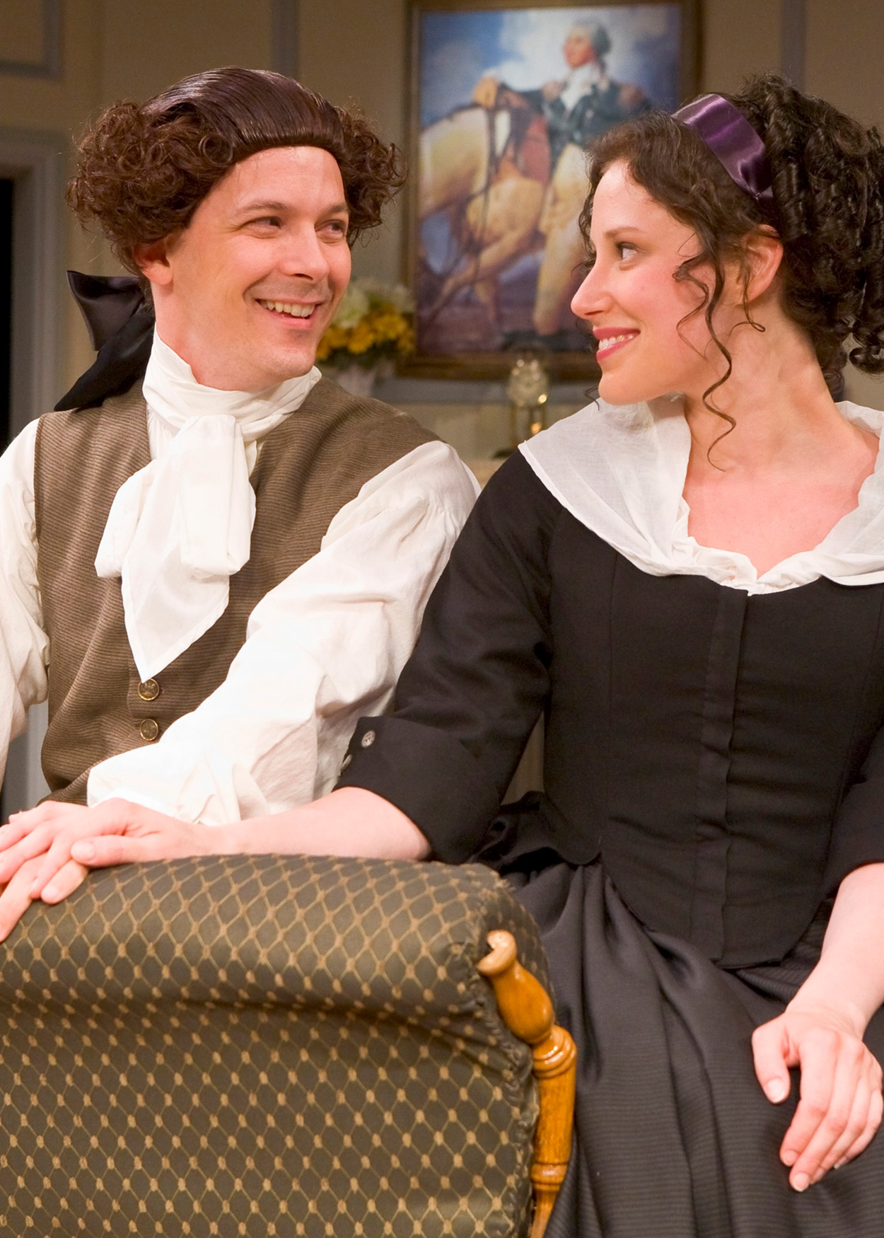 man and woman in colonial dress smile at each other