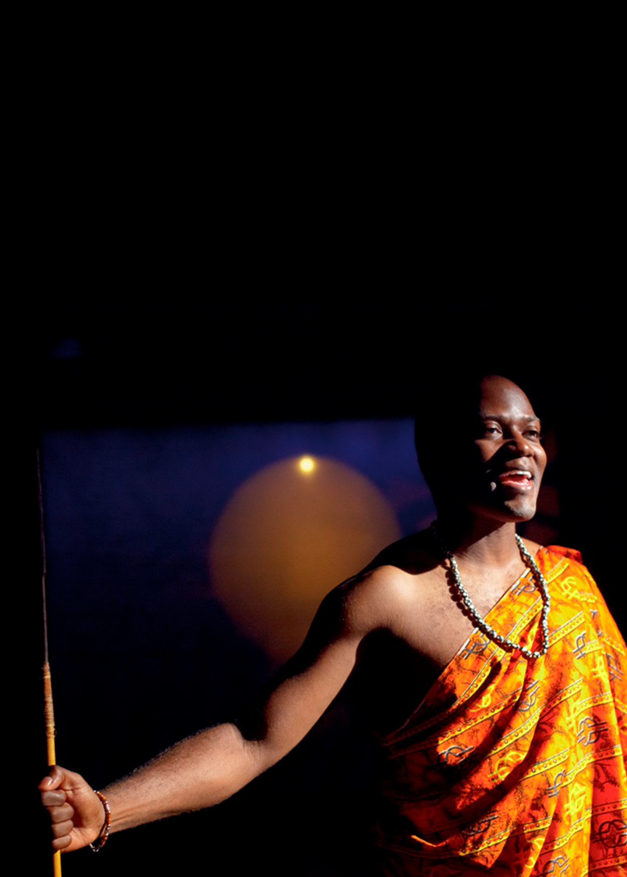African American male wearing a bright yellow African sarong arms open