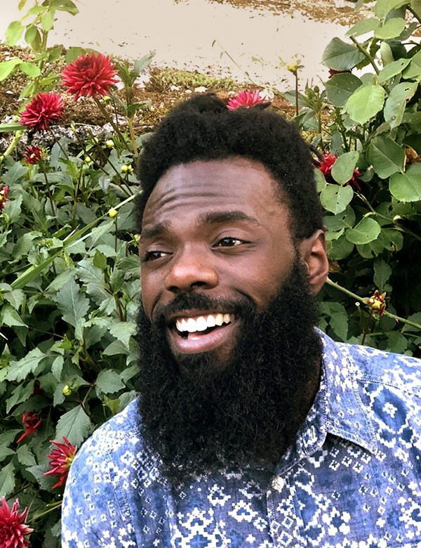 headshot of Tylie Shider, who's an African American with a beard, smiling to the side in front of roses