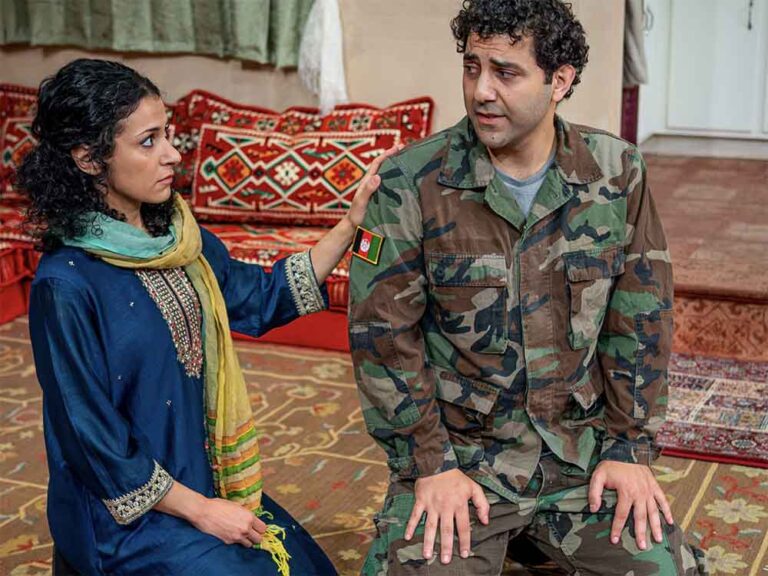Woman and man kneeling on the floor looking as if they are having a serious conversation. The man is wearing a military uniform.
