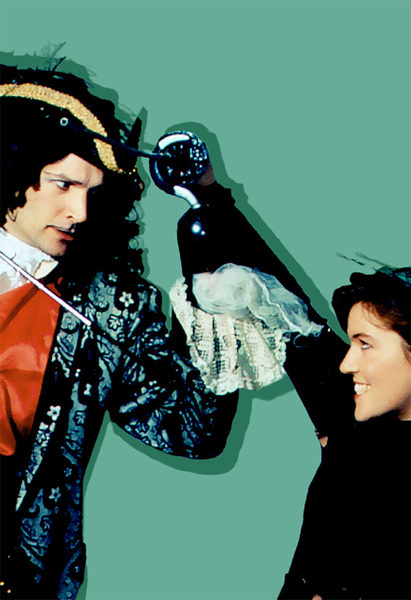 Two individuals are engaging in a playful standoff, dressed in elaborate, theatrical outfits. The scene evokes Captain Hook and Peter Pan, with vibrant costumes and a lighthearted tone of rivalry. The background is solid green, enhancing focus on the figures.