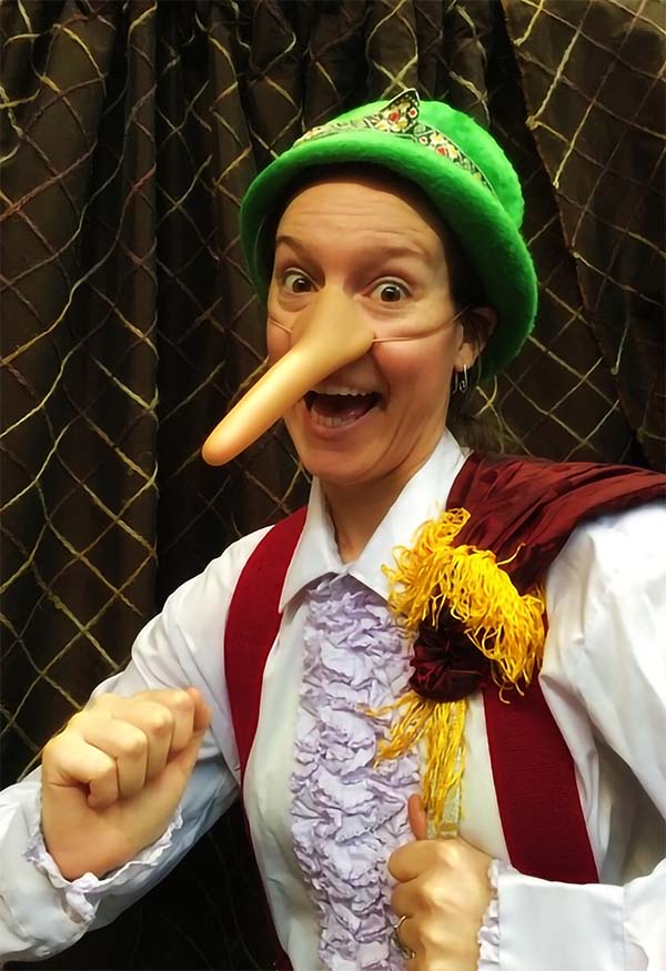 A person wearing a mock large nose and a green hat and dressed as Pinocchio from the book