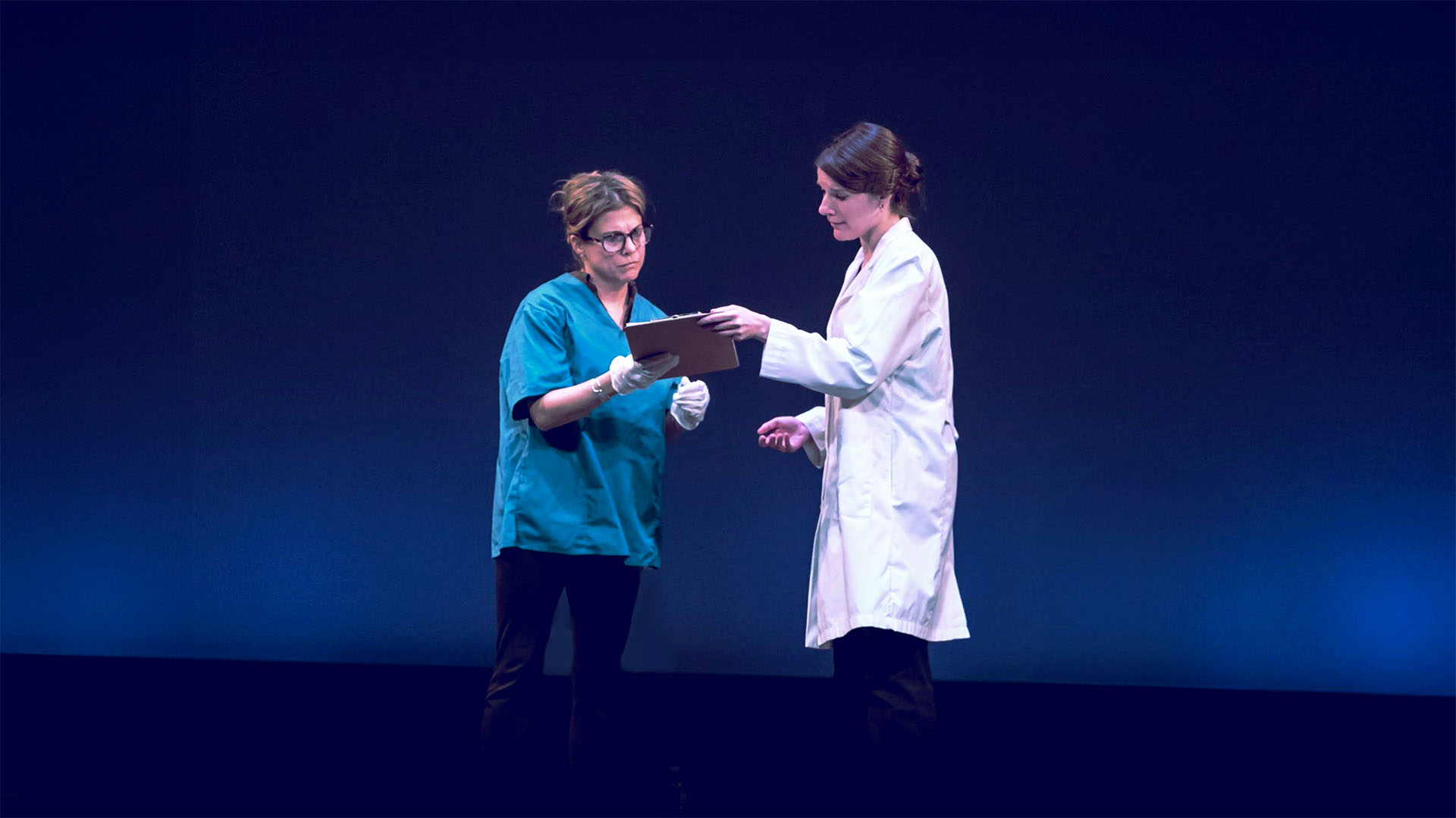 Both nurse and a doctor (females) looking at patient notes together, standing on stage
