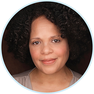 A woman with curly, dark brown hair, styled in a natural afro. She has a warm complexion, expressive brown eyes, and a gentle smile.