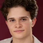 Lucas headshot wearing a light creamy shirt against a burgundy background