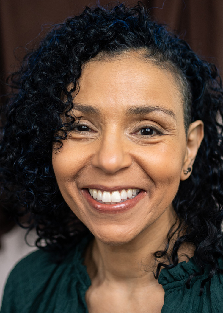 A cheerful woman with curly hair and a subtle smile, dressed in a green top against a soft, neutral background. The image conveys warmth, positivity, and approachability, capturing a moment of genuine happiness.