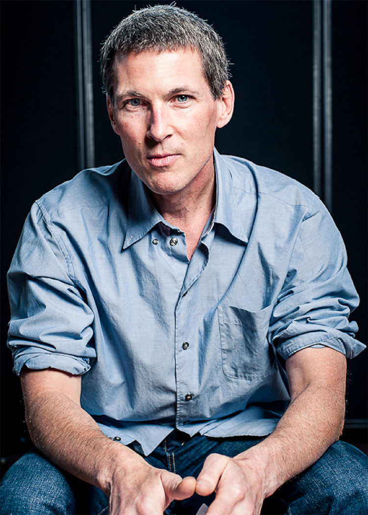 Craig is a middle-aged white male with gray hair and piercing blue eyes. He is wearing a blue button up with the sleeves rolled up above his elbows.