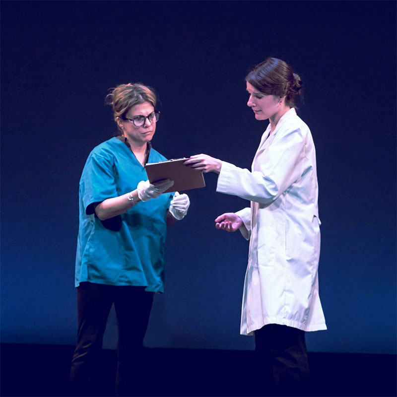 Both nurse and a doctor (females) looking at patient notes together, standing on stage