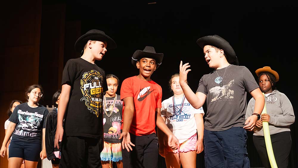 Young students dressed casually with cowboy black hats, acting on stage
